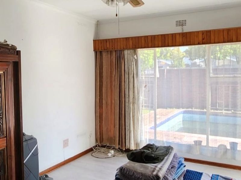 A living room featuring a ceiling fan and large window with timber pelmet, offering a view of the outdoor pool area.