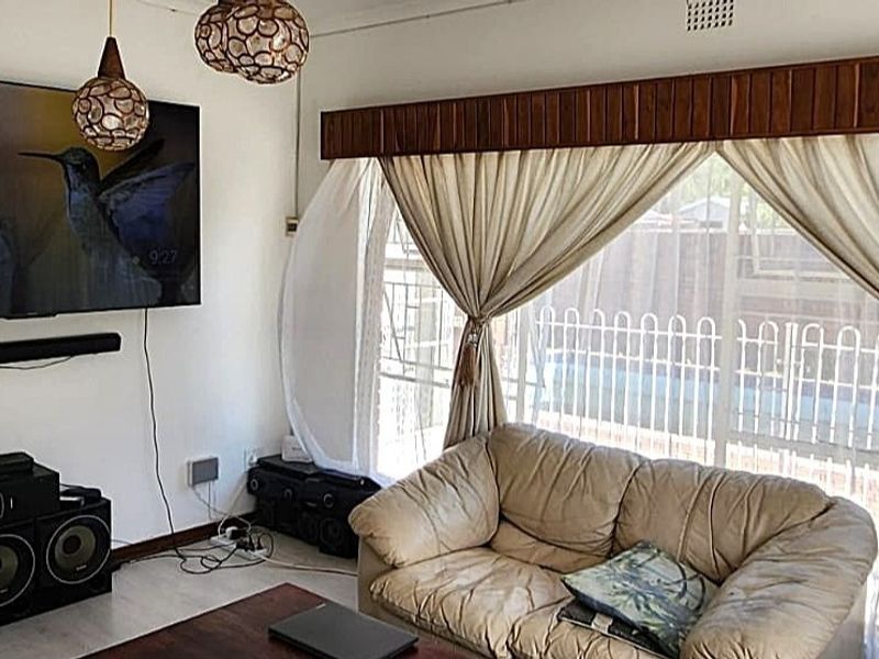 A living room featuring a large window with a wooden pelmet and security gate, providing natural light and a view of the exterior.