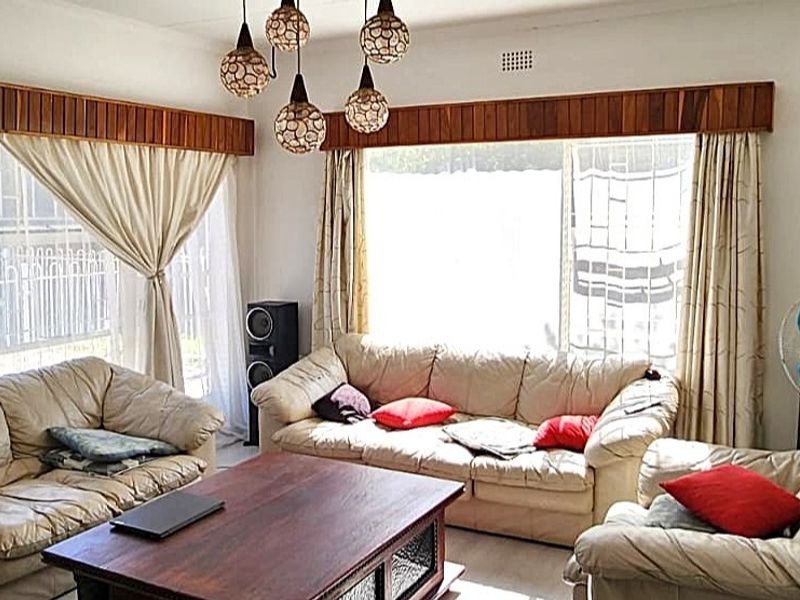 A comfortable living room featuring large windows with security bars, wooden pelmets, and decorative pendant lighting, offering a bright and functional space.