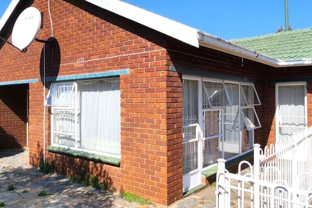 Rear exterior view of a face brick house featuring a paved patio area, aluminium window frames with security bars, and a tiled roof.