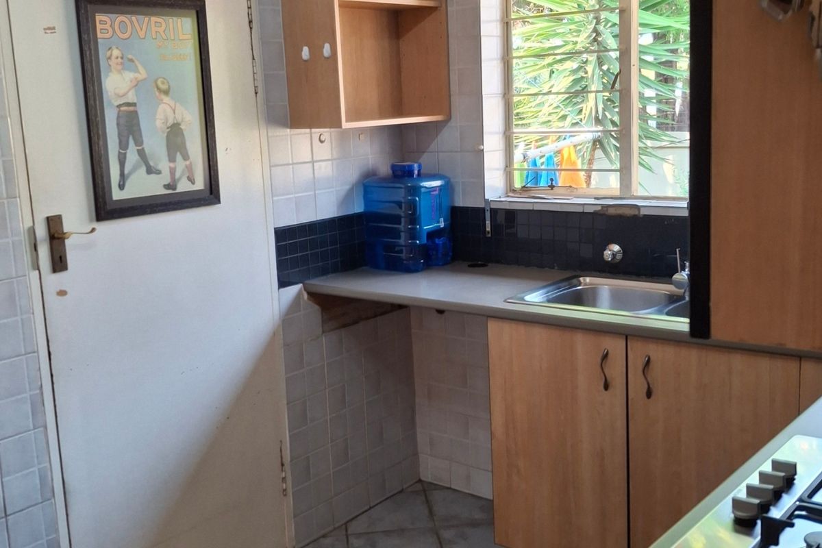 A functional kitchen area featuring built-in cabinetry, a stainless steel sink, tiled backsplash, and a built-in gas hob with security window bars.