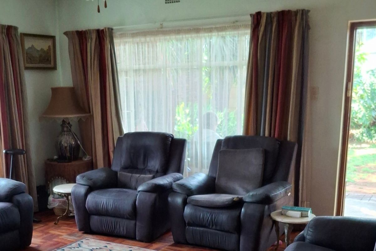 A living room featuring classic parquet flooring, large windows, and a sliding glass door providing access to the garden area.