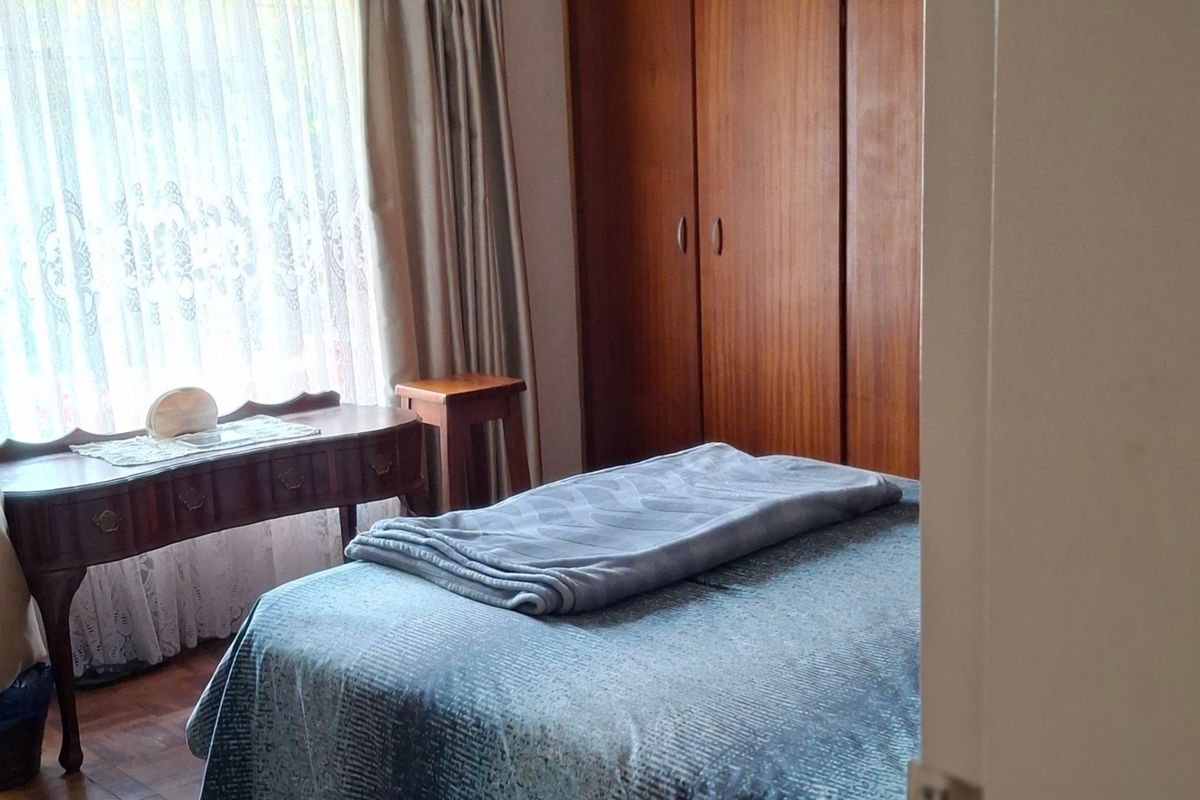 A bedroom featuring classic parquet flooring and built-in wooden cupboards, offering a traditional aesthetic with natural light.