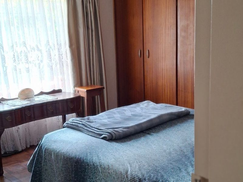 A bedroom featuring classic parquet flooring and built-in wooden cupboards, offering a traditional aesthetic with natural light.