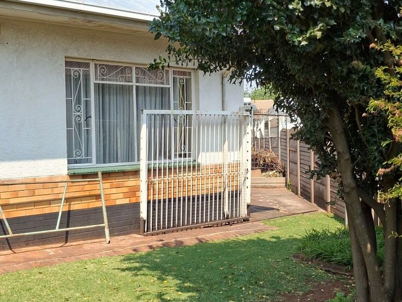 Rear exterior view of the property featuring a paved walkway, security gate, and brick facade with security bars on the windows.