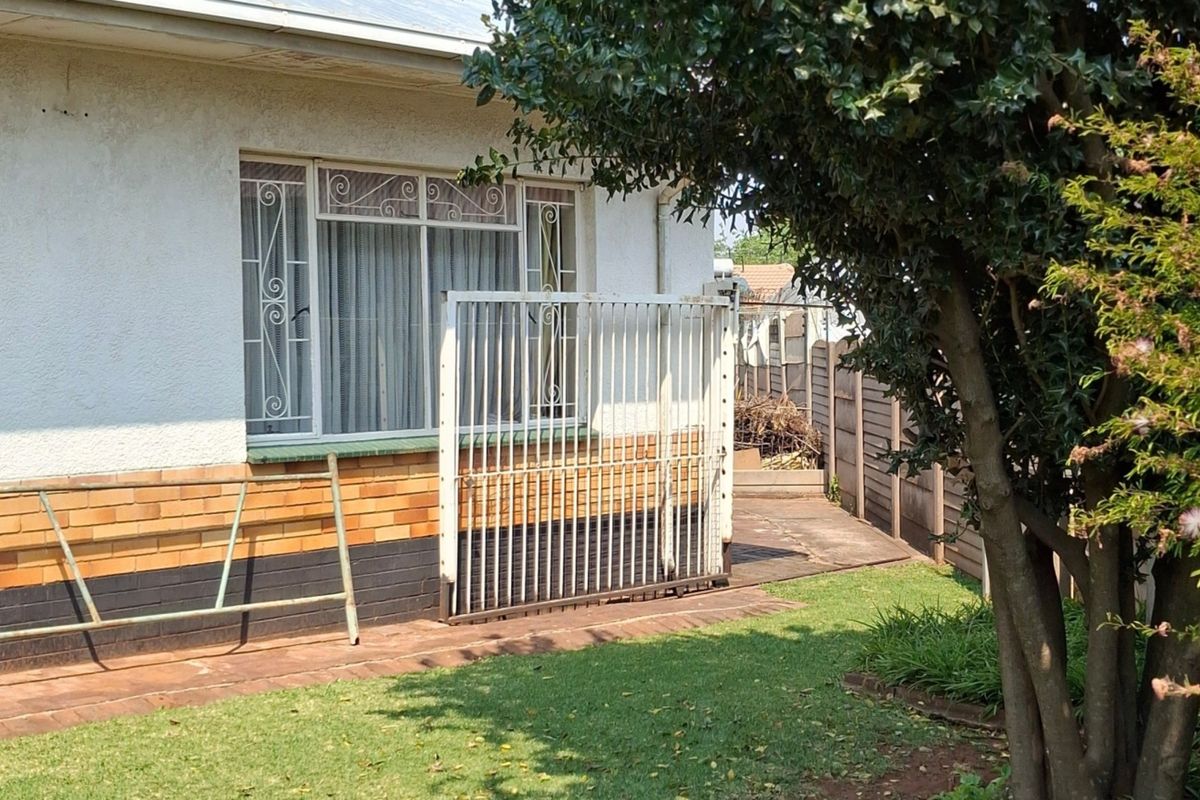 Rear exterior view of the property featuring a paved walkway, security gate, and brick facade with security bars on the windows.