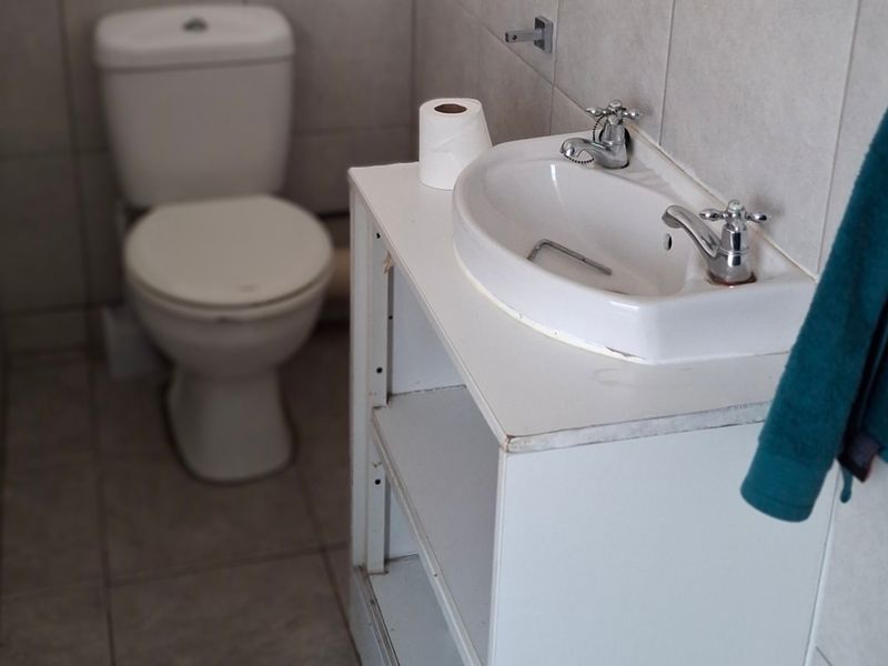 A compact bathroom featuring a standard toilet and a vanity basin with exposed shelving, finished with neutral wall and floor tiles.