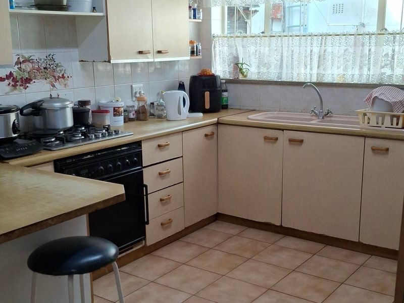 A functional kitchen featuring built-in cabinetry, laminate countertops, a gas hob, oven, and double sink with tiled flooring and backsplash.