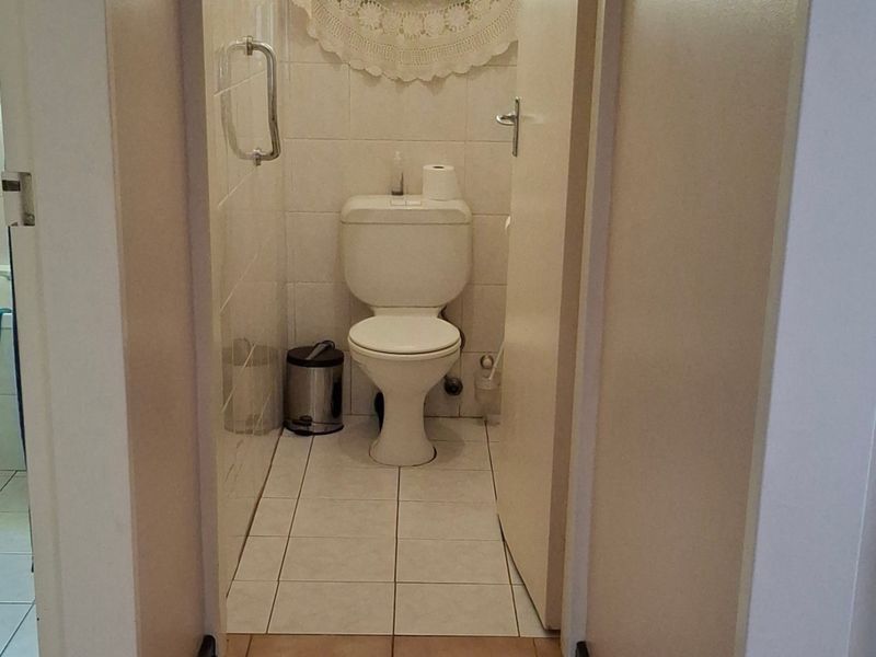 A functional bathroom featuring a standard toilet, tiled walls, and a safety grab rail, with an adjacent view into a secondary bathroom area.