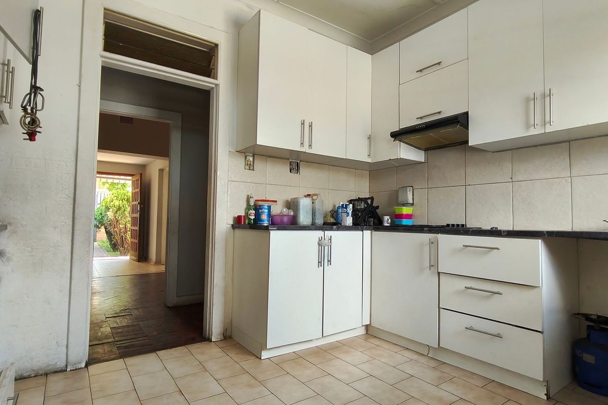 A functional kitchen featuring white cabinetry, a built-in oven, extractor fan, and tiled flooring, with direct access to an adjacent living area.