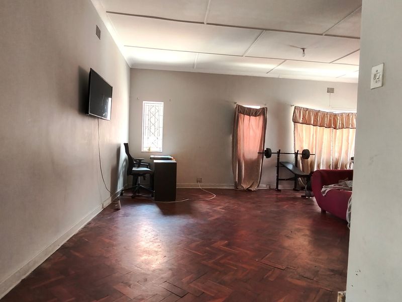 Spacious living area featuring traditional parquet flooring, large windows with security bars, and neutral wall finishes.