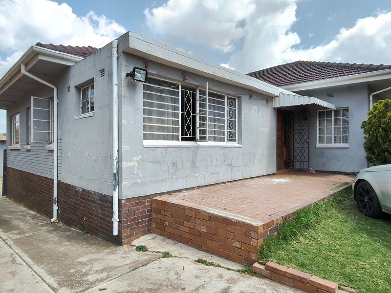 Front elevation of a single-story house featuring a brick patio, security bars on windows, and a tiled roof.