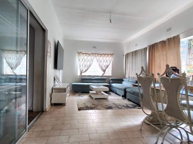 An open-plan living and dining area featuring tiled flooring, cornicing, and a large sliding glass door providing access to the exterior.