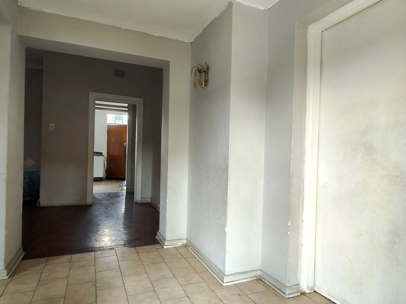 A vacant hallway featuring a transition between tiled and parquet flooring, leading into an adjacent room with a wooden door.