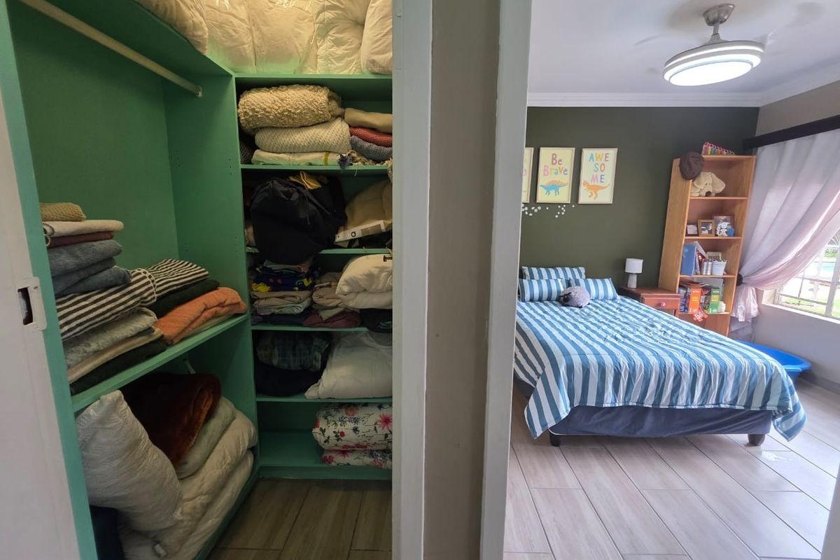 A bedroom featuring tiled flooring, a ceiling fan, and an integrated walk-in closet with built-in shelving.