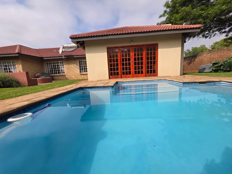 A well-maintained swimming pool area featuring a clear pool, brick exterior walls, terracotta roof tiles, and timber french doors leading to the home.