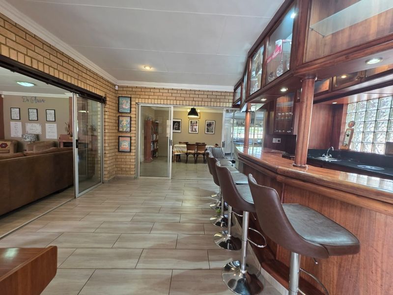 A well-appointed home bar area featuring a built-in wooden counter, glass display cabinets, and a unique glass block wall, connecting to adjacent living spaces.