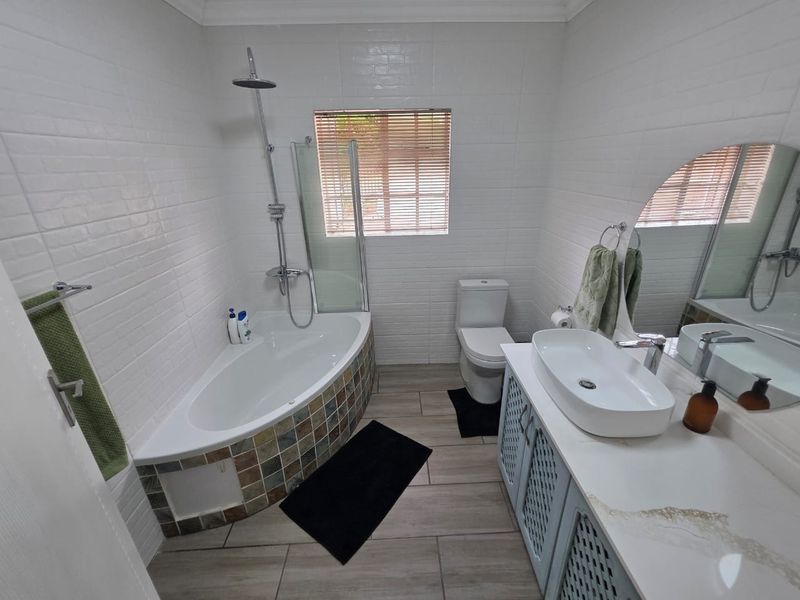 A well-maintained bathroom featuring a corner bathtub with shower attachment, a modern vessel sink on a vanity cabinet, and neutral wall and floor tiling.