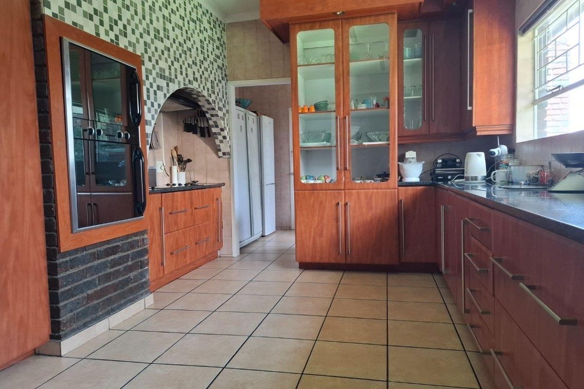Spacious kitchen featuring wood-finish cabinetry, granite countertops, built-in oven, and a distinctive brick archway feature with tiled flooring throughout.