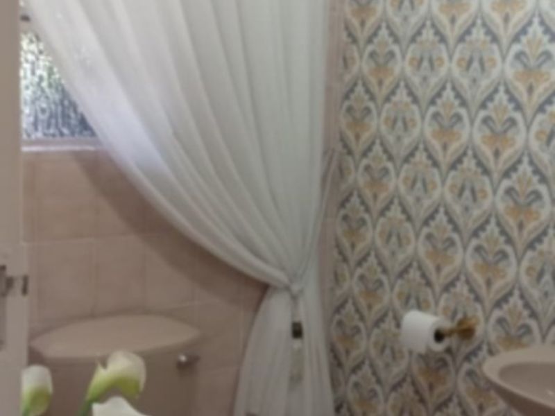 A compact bathroom featuring a toilet, pedestal basin, tiled flooring, and decorative patterned wallpaper.