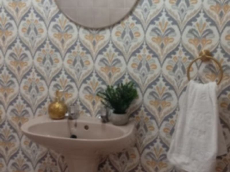 A bathroom featuring a pedestal basin, tiled flooring, and decorative patterned wallpaper with a wall-mounted mirror.