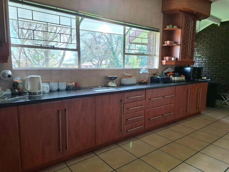 A functional kitchen featuring warm-toned built-in cabinetry, granite countertops, tiled flooring, and a large window providing natural light and garden views.