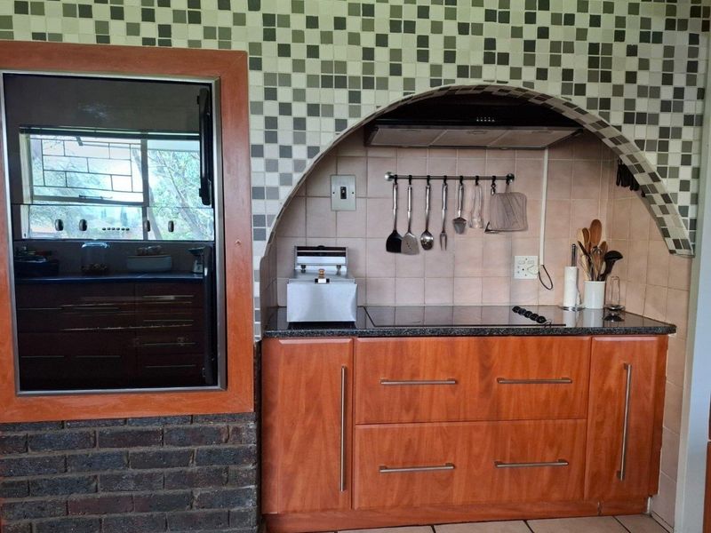 Kitchen area featuring wooden cabinetry, granite countertops, an electric hob with extractor fan, and a decorative tiled arch feature.