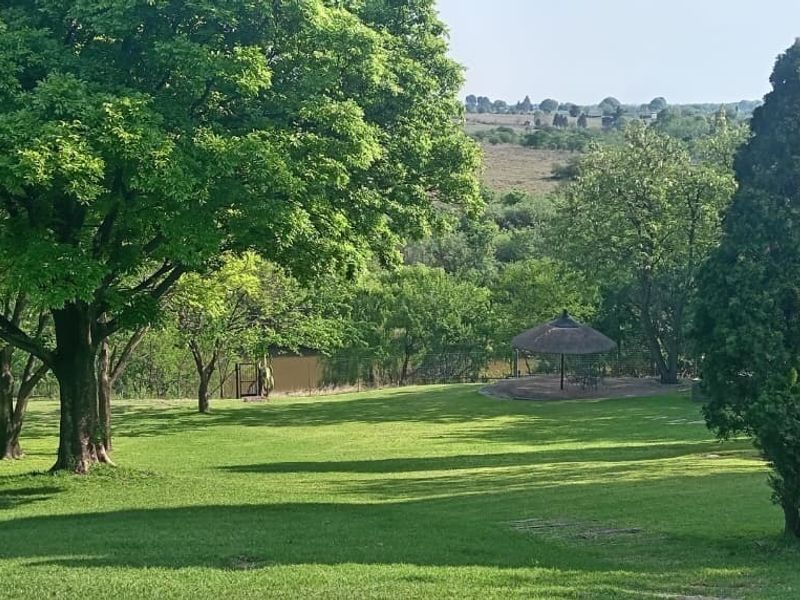 A spacious, well-maintained garden featuring mature trees, expansive lawn, and a thatched gazebo overlooking the surrounding landscape.