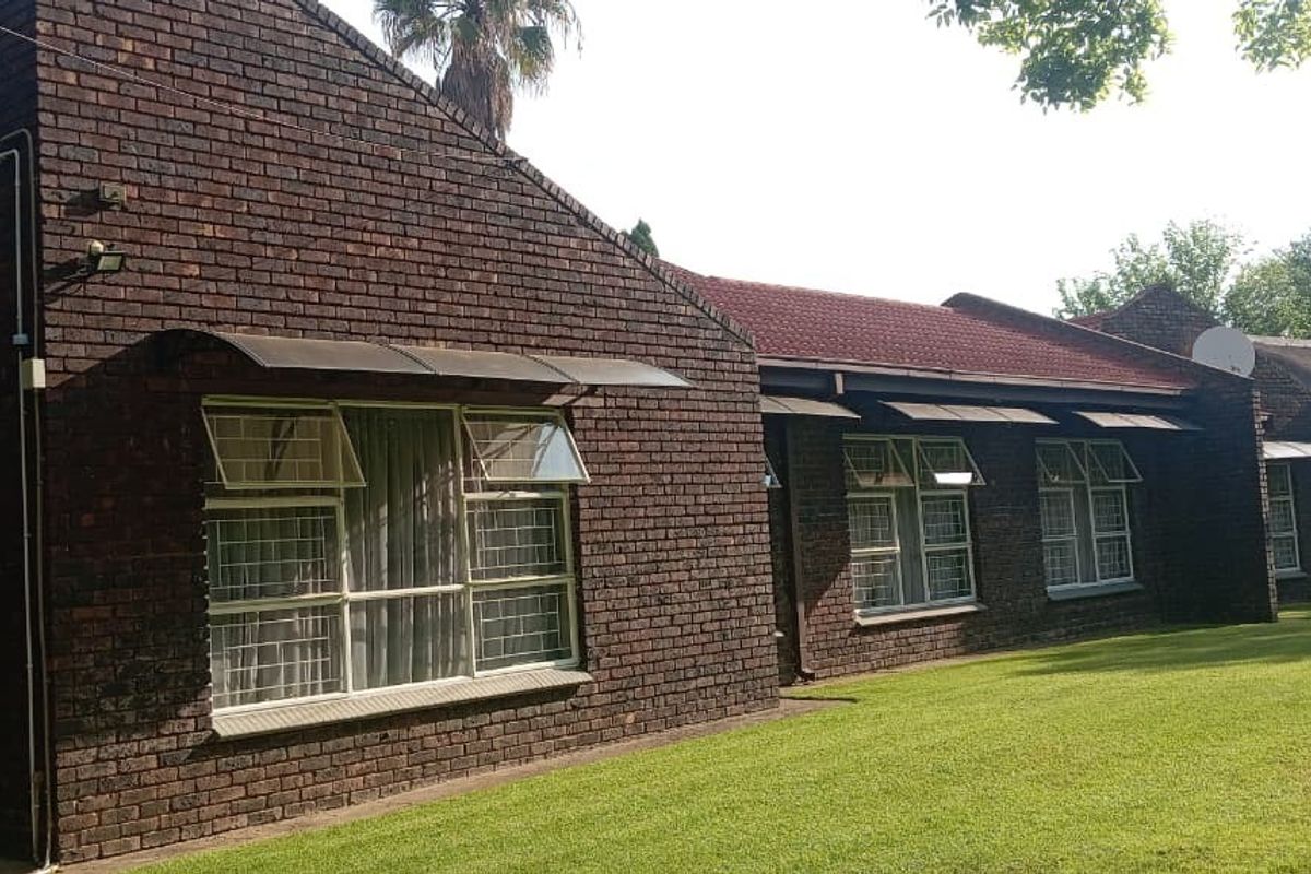 Rear view of a face brick house featuring a large lawn, steel-framed windows with awnings, and an exterior air conditioning unit.