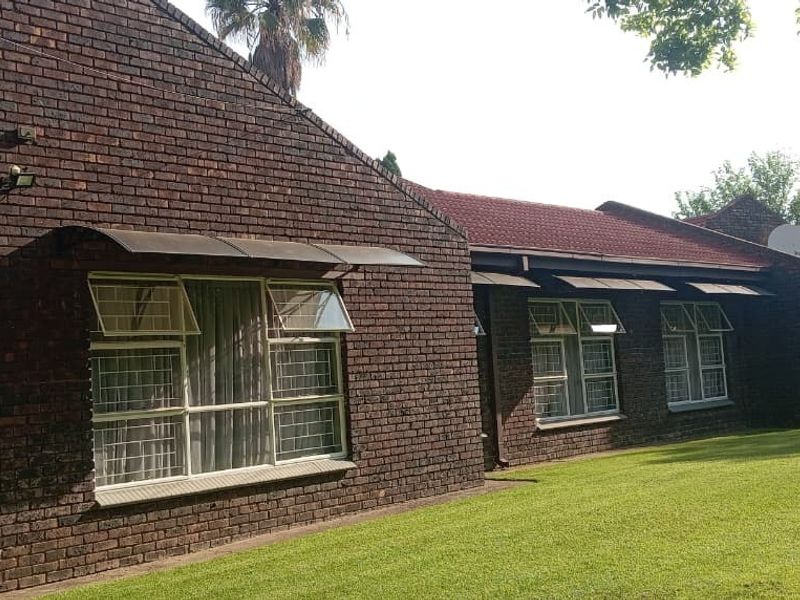 Rear view of a face brick house featuring a large lawn, steel-framed windows with awnings, and an exterior air conditioning unit.