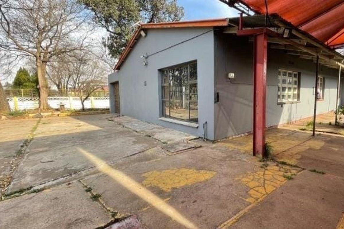 Rear exterior view of the property featuring a concrete driveway, covered patio area with steel supports, and perimeter walling.
