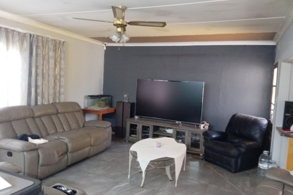 A living room featuring tiled flooring, a ceiling fan, and a dark accent wall, showing signs of ceiling water damage and unfinished trim.