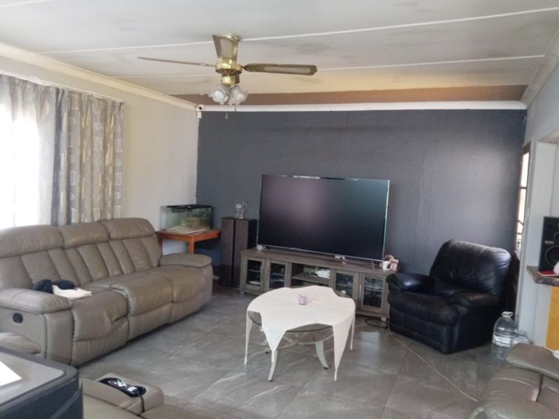 A living room featuring tiled flooring, a ceiling fan, and a dark accent wall, showing signs of ceiling water damage and unfinished trim.