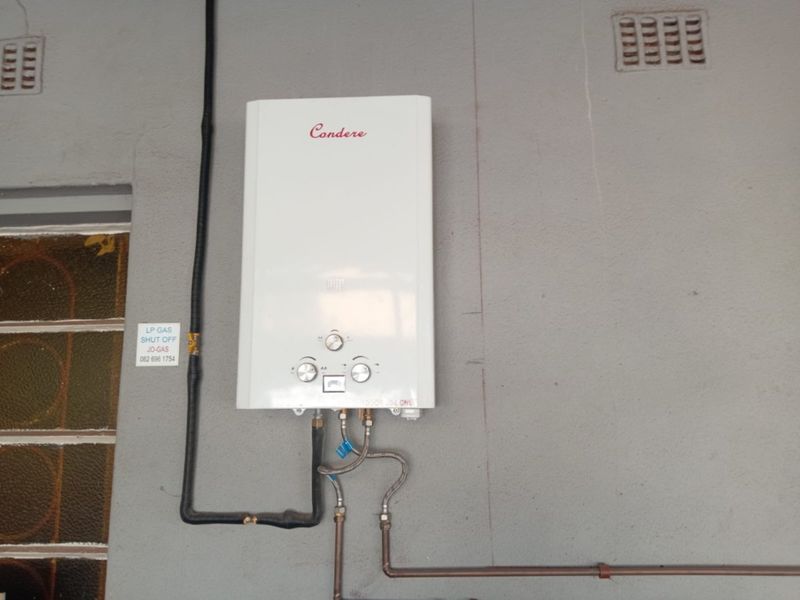 Wall-mounted gas water heater unit installed with external gas piping and safety shut-off valve.