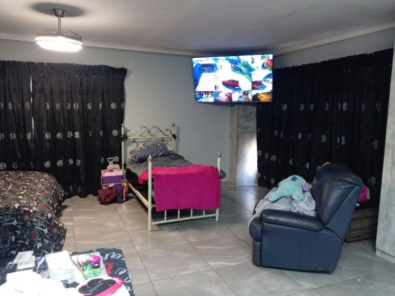 A spacious bedroom featuring tiled flooring, a ceiling fan, and a wall-mounted television, offering a functional layout for rest and relaxation.