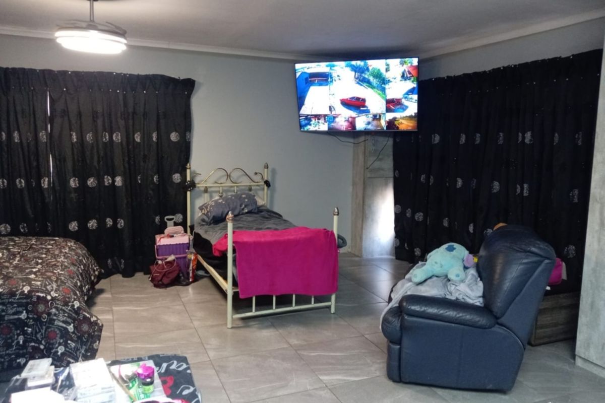 A spacious bedroom featuring tiled flooring, a ceiling fan, and a wall-mounted television, offering a functional layout for rest and relaxation.