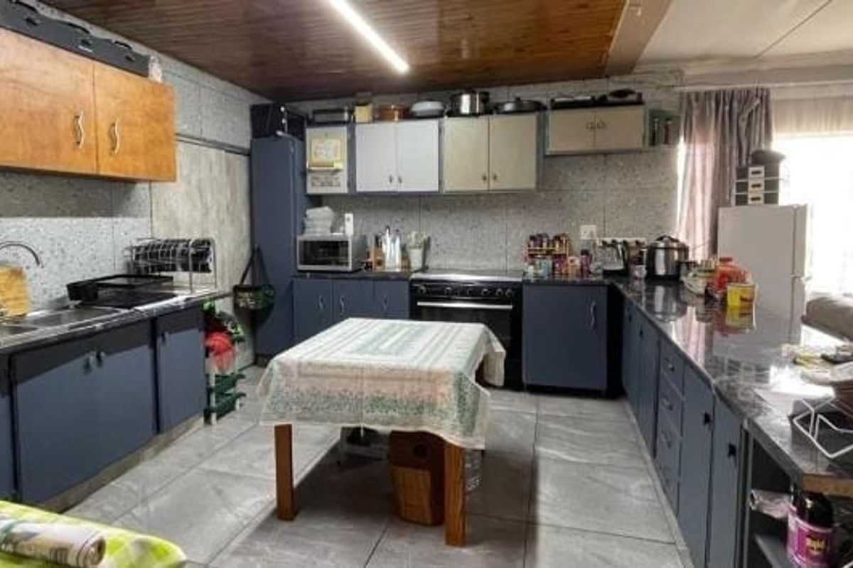 A functional kitchen featuring extensive built-in cabinetry, laminate countertops, a stainless steel sink, and a freestanding oven, with traditional timber ceiling paneling.