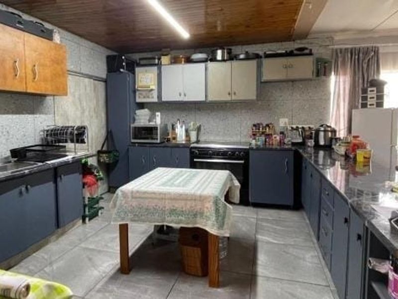 A functional kitchen featuring extensive built-in cabinetry, laminate countertops, a stainless steel sink, and a freestanding oven, with traditional timber ceiling paneling.