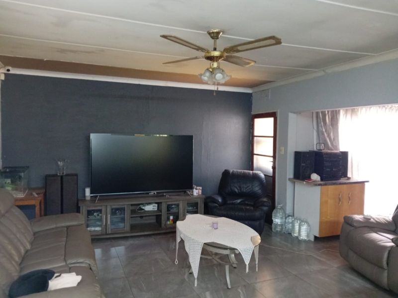 Living room featuring tiled flooring, a ceiling fan, and built-in cabinetry, with visible signs of ceiling water damage requiring attention.