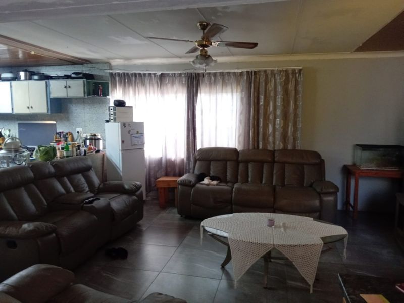 Open plan living and kitchen area featuring tiled flooring and a ceiling fan, requiring cosmetic updates to the ceiling and finishes.