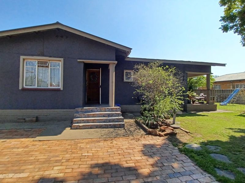 Front elevation of a single-story house featuring a brick driveway, covered entrance porch, and established garden area.