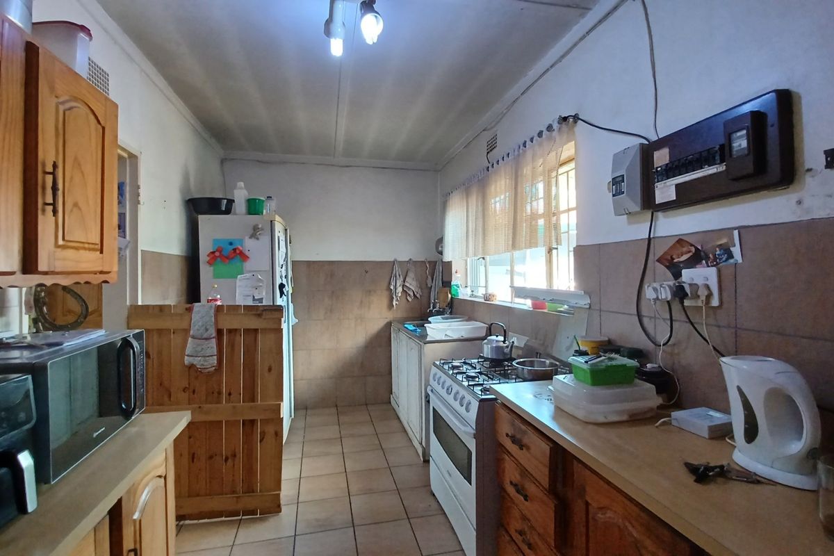 A functional kitchen featuring wooden cabinetry, a gas stove, tiled splashbacks, and tiled flooring, offering potential for modernization and aesthetic improvement.