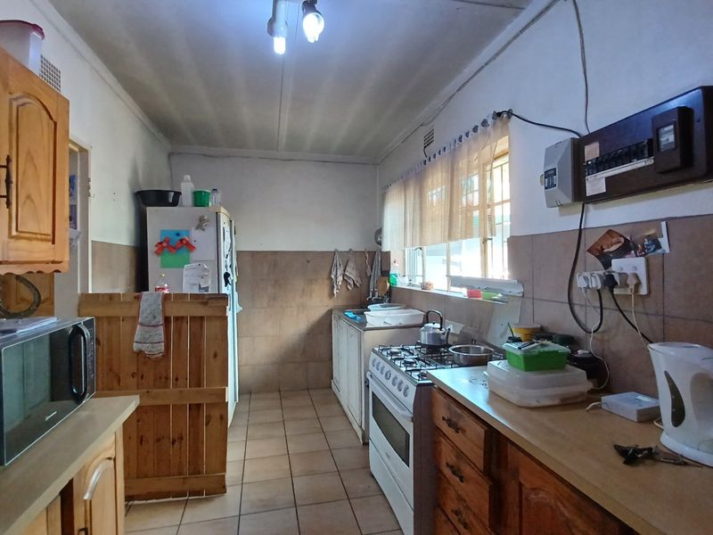 A functional kitchen featuring wooden cabinetry, a gas stove, tiled splashbacks, and tiled flooring, offering potential for modernization and aesthetic improvement.