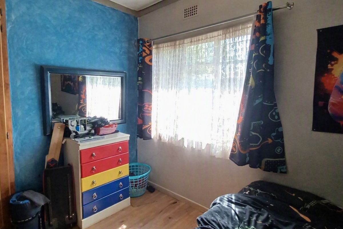 A bedroom featuring laminate flooring, a built-in wardrobe, and a wall-mounted air vent, offering a functional space with potential for modernization.