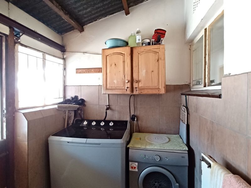A functional laundry area featuring tiled walls, timber cabinetry, and exposed rafter ceiling, providing a practical space for washing and utility tasks.