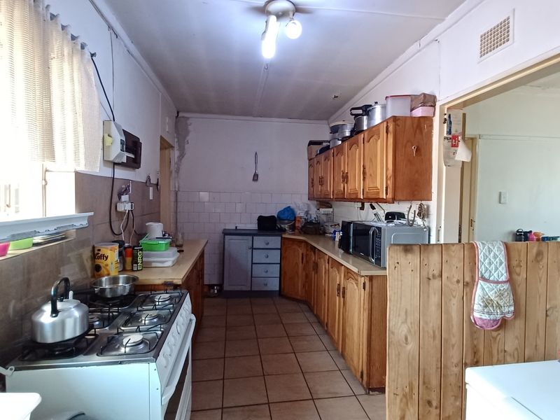A functional kitchen featuring wooden cabinetry, tiled splashbacks, and a gas stove, offering a practical layout with potential for modern cosmetic updates.