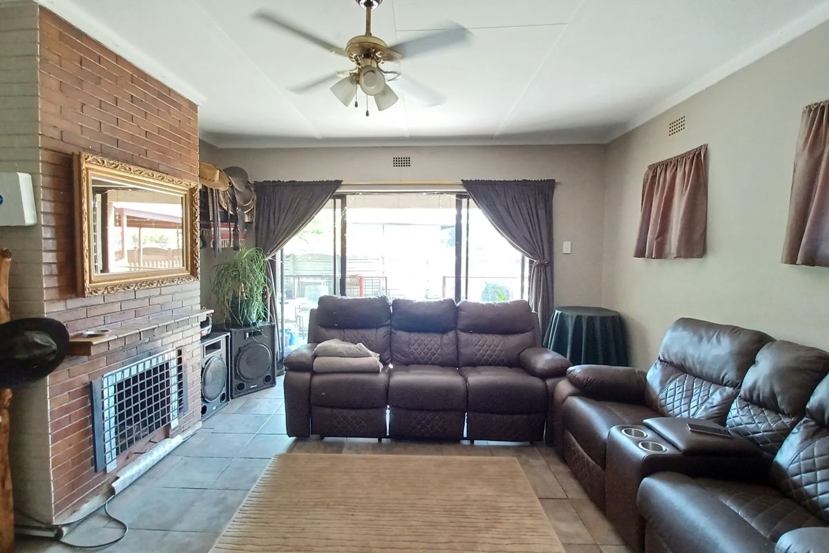 A living room featuring a brick fireplace, tiled flooring, and a ceiling fan, with sliding glass doors providing access to the outdoor area.