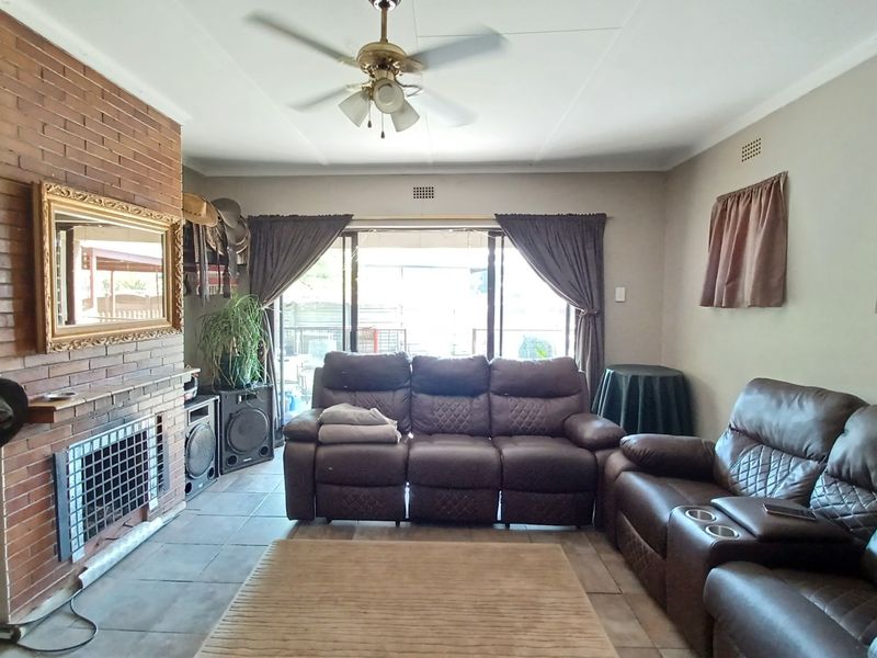 A living room featuring a brick fireplace, tiled flooring, and a ceiling fan, with sliding glass doors providing access to the outdoor area.