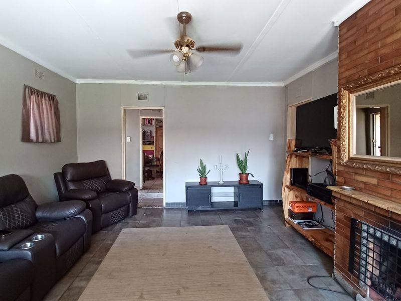 A living room featuring tiled flooring, a brick fireplace, and a ceiling fan, offering a functional space with potential for modern updates.
