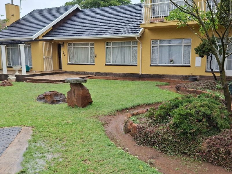 Front view of a single-story house featuring a tiled roof, covered patio, balcony, and a landscaped garden with a paved driveway.